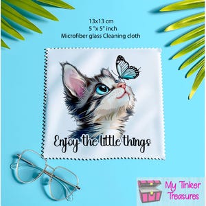 Könnte beinhalten: Ein weißes Mikrofaser-Reinigungstuch mit einem blauen Schmetterling und einem Kätzchen, das nach oben schaut. Das Tuch ist 13 cm x 13 cm groß und hat den Text "Enjoy the little things" aufgedruckt.