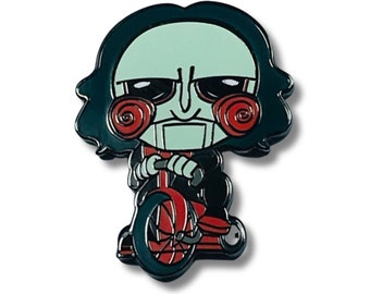 May include: Black and green enamel pin of a cartoon character with a red and black tricycle. The character has a green face, black hair, and red and black spiral saw blades for ears.