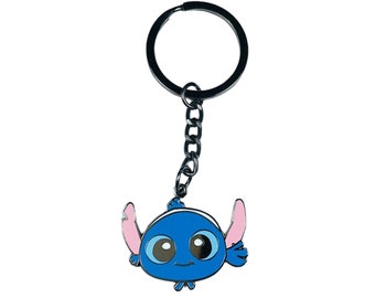 May include: A blue character keychain with large eyes and pink ears. The keychain has a silver chain and a round key ring. The character is a cartoon alien. The keychain is a collectible item.