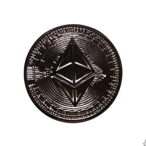 May include: A silver-colored Ethereum cryptocurrency coin with a geometric design in the center. The coin has a raised rim and a textured surface.