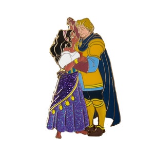 Op de afbeelding: Een gouden emaille pin met een dansend cartoon-koppel. De vrouw draagt een paars-gouden jurk en de man draagt een geel-blauwe outfit.