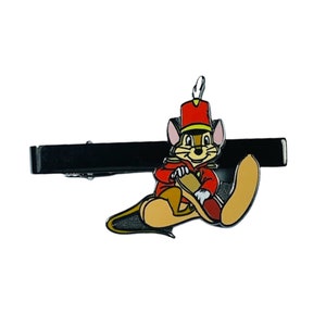 以下が含まれることがあります： 赤い金色の制服を着た漫画のネズミが描かれた黒い金属製のネクタイピン。ネズミはドラムスティックを持っており、帽子には羽根がついています。