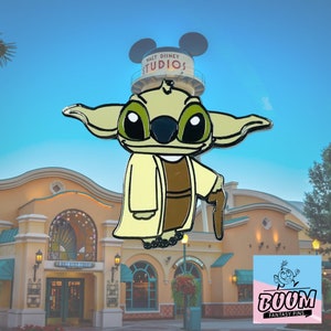 May include: A green and brown enamel pin featuring a cartoon character with large eyes and ears, wearing a brown robe and holding a walking stick. The pin is in front of a building with the text "WALT DISNEY STUDIOS" on it. The pin is labeled "BOOM FANTASY PINS".
