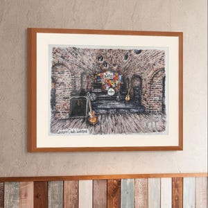 Puede incluir: Obra de arte enmarcada que representa el Cavern Club de Liverpool, con un escenario con instrumentos musicales y un letrero de "Beatles". La obra está en un marco de madera y cuelga de una pared con un panel decorativo de madera en la parte inferior. El texto "Cavern Club Liverpool" es visible.