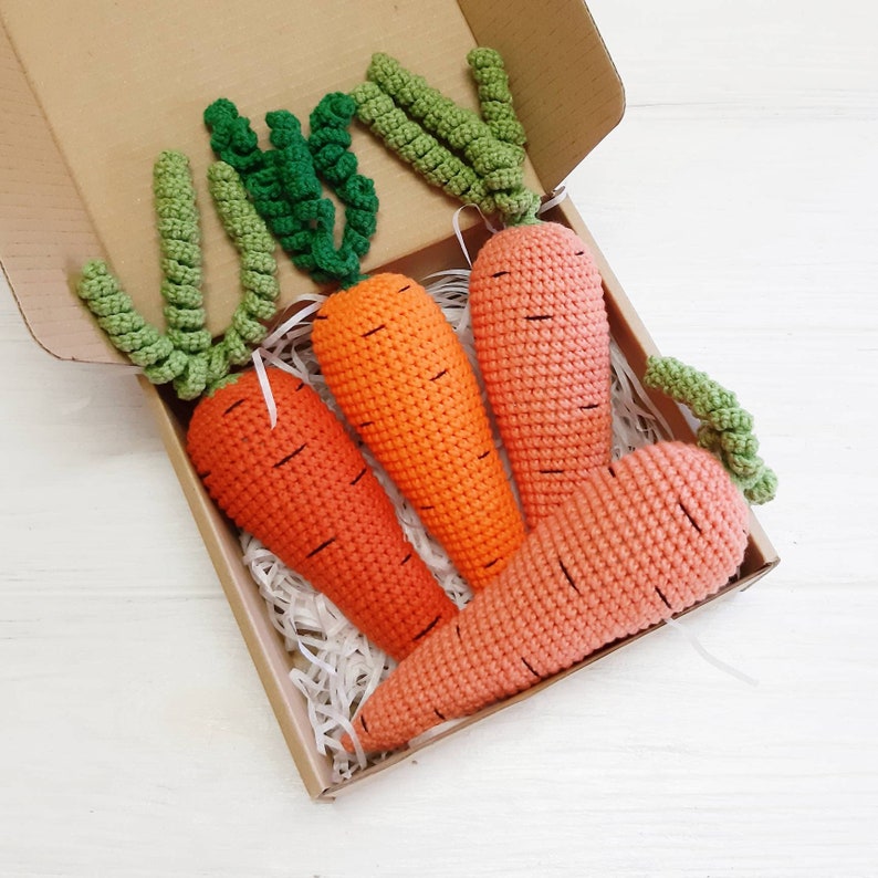 May include: Four crocheted carrots in a brown box with white tissue paper. The carrots are orange and have green tops.