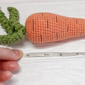 May include: A crocheted carrot toy with green leaves, measuring 12.7 cm long. The carrot is orange with black lines and the leaves are green.