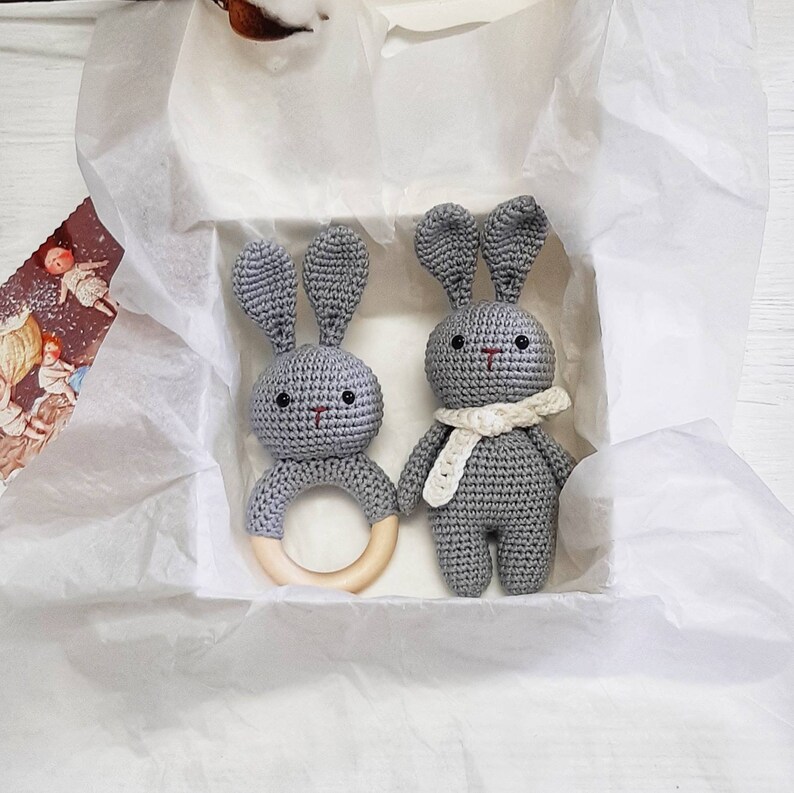 Puede incluir: Dos juguetes de conejo de crochet gris con anillos de dentici&oacute;n de madera. Un conejo lleva una bufanda de crochet blanca.