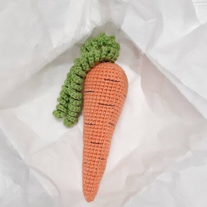 May include: A crocheted carrot toy with a green leafy top. The carrot is orange and has black stitching for detail.