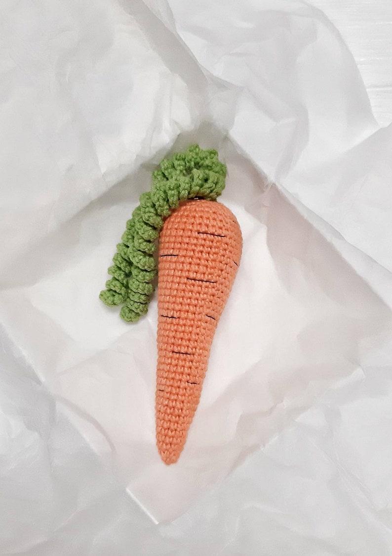 May include: A crocheted carrot toy with a green leafy top. The carrot is orange and has black stitching for detail.