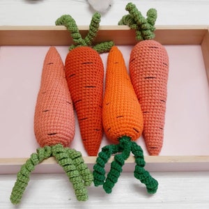 May include: Four crocheted carrots in a wooden tray with a pink liner. The carrots are orange and pink with green tops.