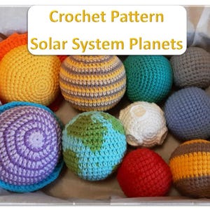 Puede incluir: Una colección de nueve objetos esféricos de ganchillo que representan los planetas del sistema solar, incluyendo un sol amarillo, una tierra azul y verde, y una luna blanca, con un letrero Crochet Pattern Solar System Planets en una caja.