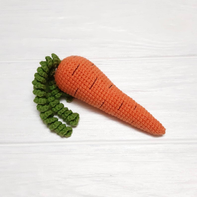 May include: A crocheted carrot toy with a green leafy top. The carrot is orange with black lines and the leaves are green.