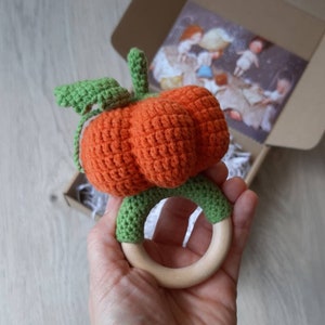 May include: A crocheted orange pumpkin with green leaves attached to a wooden teething ring.