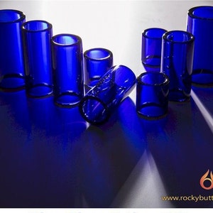 May include: A set of eight blue glass guitar slides of varying sizes. The slides are arranged on a white surface.