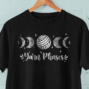 May include: Black t-shirt with a silver graphic of yarn balls and moons with the text "Yarn Phases".