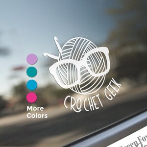 May include: White vinyl decal with a yarn ball wearing glasses and the text "Crochet Geek". The decal is on a car window.  The text "Green Fox Farms Designs" is also visible on the window.