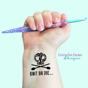 May include: A black and white temporary tattoo with a yarn ball skull and crossbones design. The tattoo says "Knit or Die..." and "Green Fox Farms Designs".