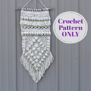 May include: A white crochet wall hanging with a variety of textures and fringe. The hanging is attached to a wooden dowel and has a "Crochet Pattern ONLY" label.