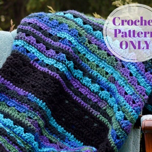 Op de afbeelding: Een handgemaakte gehaakte deken in tinten zwart, paars, blauw en groen, gedrapeerd over een lichtblauwe stoel. De deken heeft een textuurpatroon en de tekst "Crochet Pattern ONLY" in een cirkelvormige afbeelding.