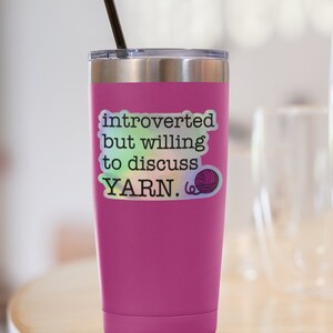 May include: Pink stainless steel tumbler with a black straw and a sticker that says "introverted but willing to discuss YARN." The sticker has a holographic finish and a small yarn ball graphic.