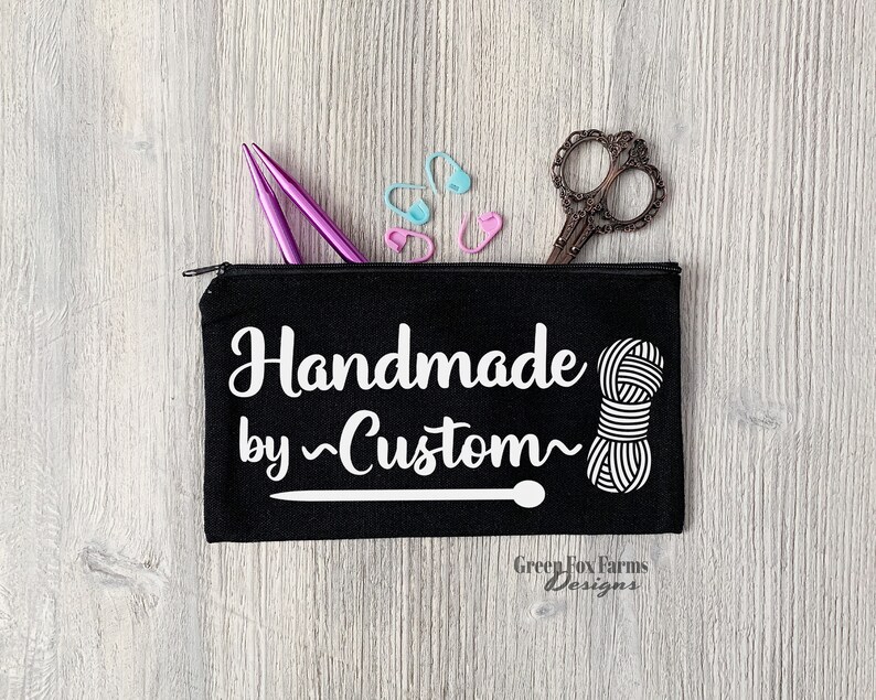 May include: Black zippered pouch with the text "Handmade by ~Custom~" in white, a white yarn ball, and a knitting needle. The pouch also has the text "Green Fox Farms Designs" in white.
