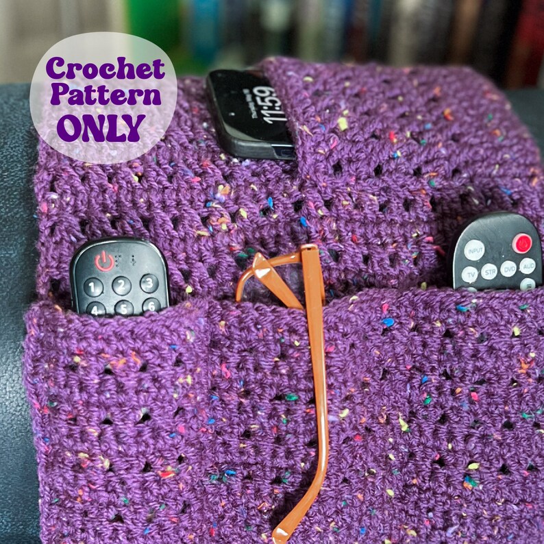 May include: Purple crochet couch caddy with pockets for remotes, glasses, and other items. The caddy has a speckled pattern and is crocheted with a single crochet stitch.