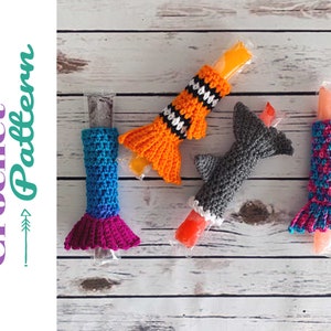 May include: Four crocheted popsicle covers in different designs: a mermaid, a shark, a clownfish, and a pink and blue fish. The covers are made with colourful yarn and are perfect for keeping popsicles cold and preventing drips.