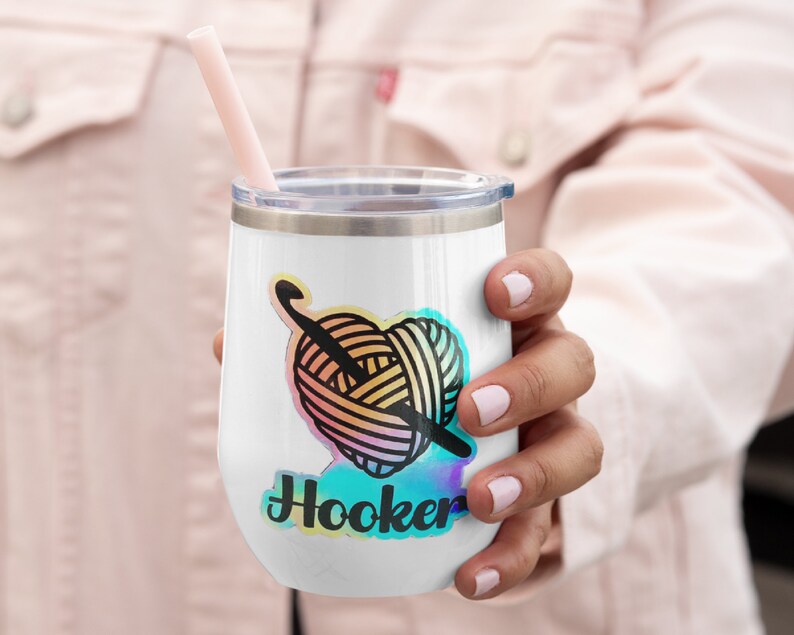 May include: White stainless steel wine tumbler with a colourful yarn ball and crochet hook design and the text "Hooker" in a rainbow font.