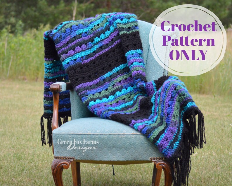Op de afbeelding: Een handgemaakte gehaakte deken in tinten zwart, teal, paars en groen, gedrapeerd over een vintage blauwe stoel. De deken heeft een gestreept patroon en franjes. De tekst "Crochet Pattern ONLY" staat in een witte cirkel.