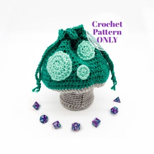 May include: Crochet pattern for a green and grey mushroom-shaped dice bag. The bag is sitting on a white surface with several iridescent dice scattered around it. The text "Crochet Pattern ONLY" is written in a purple circle above the bag.