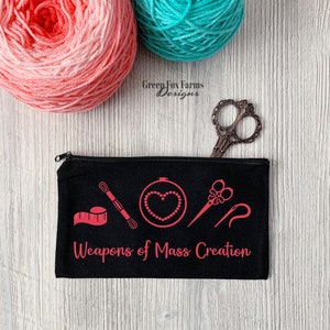 May include: Black zippered pouch with the text "Weapons of Mass Creation" in pink. The pouch has a pink design of sewing tools, including a needle, thread, scissors, and a tape measure.