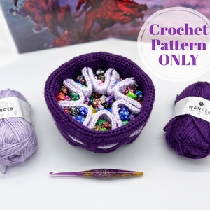 Puede incluir: Bolsa de dados de crochet morado con un dise&ntilde;o en forma de estrella. La bolsa est&aacute; llena de dados de colores. La imagen tambi&eacute;n muestra hilo morado y un gancho de crochet.