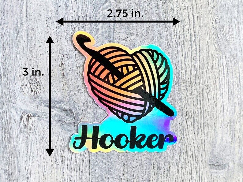 May include: A holographic sticker featuring a rainbow yarn ball and crochet hook, with the word "Hooker" in black text.