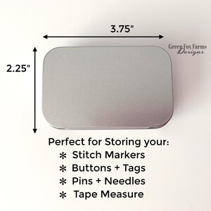 May include: A silver metal tin with a rounded rectangular shape. The tin is 3.75 inches wide and 2.25 inches tall. The text "Perfect for Storing your:" is printed below the tin. The text "* Stitch Markers" is printed below the text "Perfect for Storing your:". The text "* Buttons + Tags" is printed below the text "* Stitch Markers". The text "* Pins + Needles" is printed below the text "* Buttons + Tags". The text "* Tape Measure" is printed below the text "* Pins + Needles". The text "Green Fox Farms Designs" is printed in the top right corner of the image.
