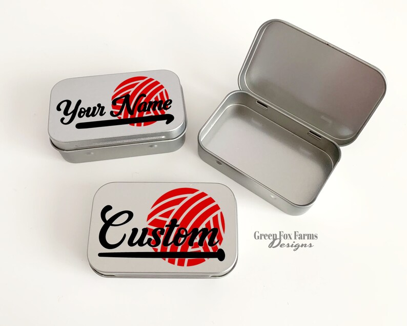 May include: Two silver metal tins with a red and white yarn ball and knitting needle design. One tin says "Your Name" and the other says "Custom". The bottom tin has the text "Green Fox Farms Designs".