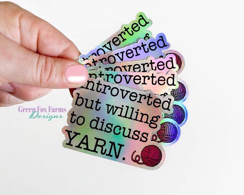 May include: A stack of iridescent holographic stickers with the text "Introverted but willing to discuss YARN."  The stickers feature a small yarn ball graphic.