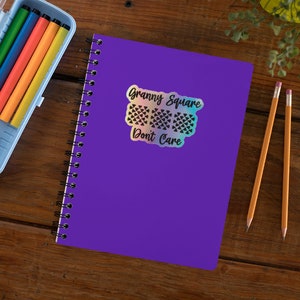 May include: A purple notebook with a holographic sticker that says "Granny Square Don't Care". The sticker features a black and white design of three granny squares.
