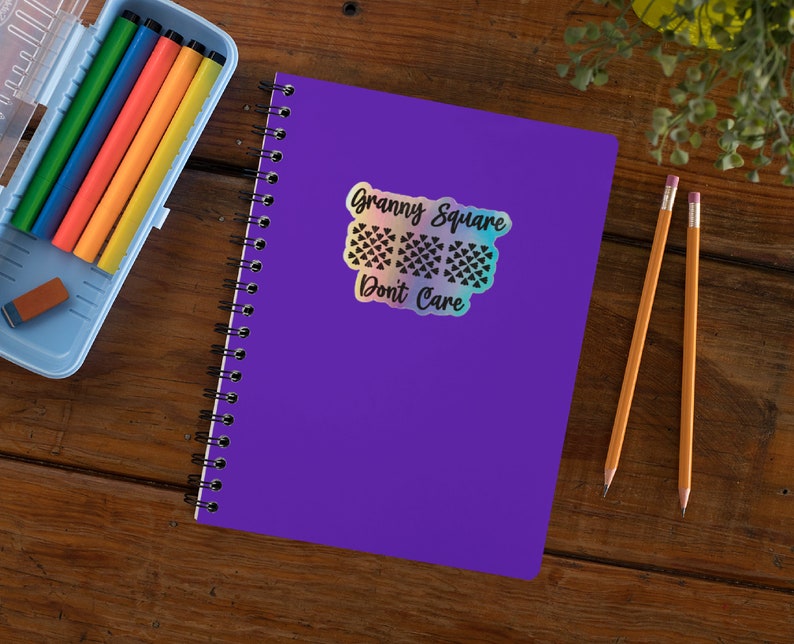 May include: A purple notebook with a holographic sticker that says "Granny Square Don't Care". The sticker features a black and white design of three granny squares.