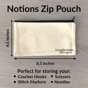 May include: A beige canvas zip pouch with a black zipper and black trim. The pouch measures 8.5 inches by 4.5 inches and has the text "Green Fox Farms Designs" printed on the bottom. The pouch is perfect for storing crochet hooks, scissors, stitch markers, and needles.