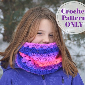 May include: A crocheted cowl in shades of purple, pink, and blue. The cowl is worn around the neck and is made with a textured stitch pattern. The image includes the text "Crochet Pattern ONLY" in a circular graphic.