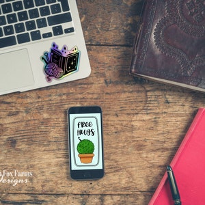 May include: A smartphone with a black case and a white screen displaying a green plant in a pot with the text "free hugs" on a wooden surface.