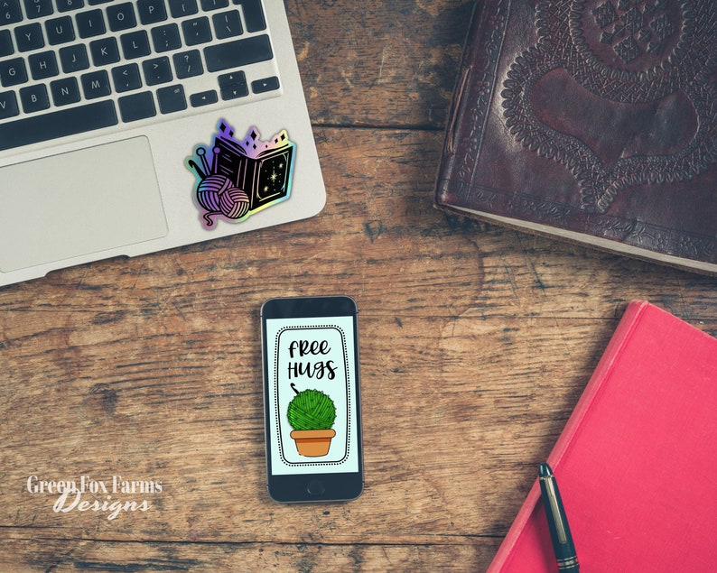 May include: A smartphone with a black case and a white screen displaying a green plant in a pot with the text "free hugs" on a wooden surface.