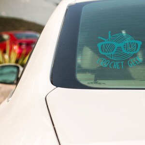 May include: A teal blue car window sticker with a ball of yarn, knitting needles, and glasses. The text "crochet geek" is below the yarn ball.