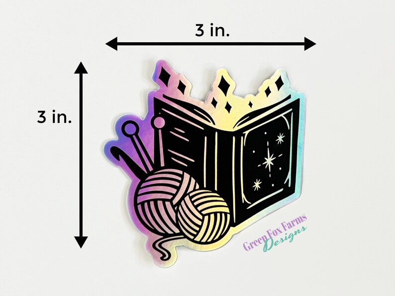 May include: A 3-inch by 3-inch iridescent sticker featuring a black and white illustration of an open book with stars and a ball of yarn with knitting needles. The sticker has the text "Green Fox Farms Designs" at the bottom.