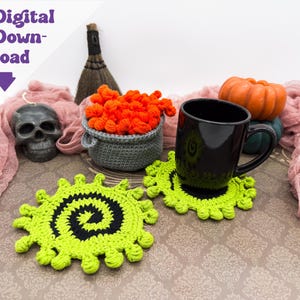 May include: A Halloween-themed still life featuring a black mug on a green and black crochet coaster. Other items include a skull, a cauldron with orange yarn, and a pumpkin. The words "Digital Download" are in the upper left corner.