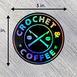 May include: A 3-inch round sticker with a black background and a holographic finish. The sticker features a white design of crossed crochet hooks with coffee beans, surrounded by the text "CROCHET & COFFEE".
