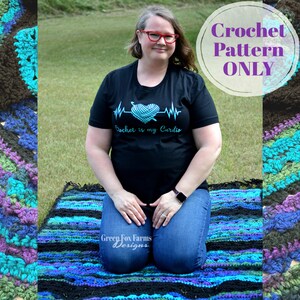 Op de afbeelding: Een vrouw draagt een zwart t-shirt met de tekst "Crochet is my Cardio" en een gehaakt hartontwerp. Ze knielt op een kleurrijke, gestreepte gehaakte deken. De afbeelding bevat ook een haakpatroonafbeelding.
