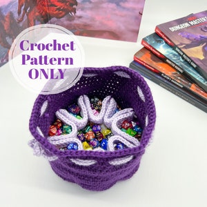 Puede incluir: Bolsa de dados de ganchillo morado con ribete de ganchillo blanco. La bolsa est&aacute; llena de dados de colores. El texto "Crochet Pattern ONLY" est&aacute; escrito en blanco sobre un c&iacute;rculo morado.