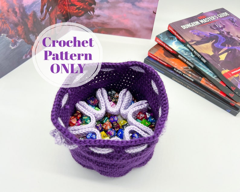 Puede incluir: Bolsa de dados de ganchillo morado con ribete de ganchillo blanco. La bolsa est&aacute; llena de dados de colores. El texto "Crochet Pattern ONLY" est&aacute; escrito en blanco sobre un c&iacute;rculo morado.