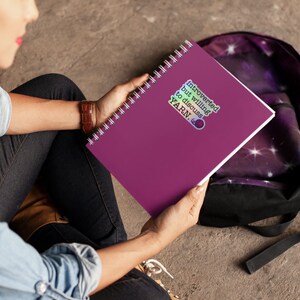 May include: A purple spiral bound notebook with a sticker that says "Introverted but willing to discuss YARN."